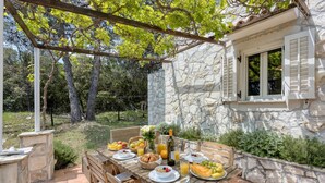 Un espace de restauration en plein air avec des murs en pierre, une pergola et une table dressée avec des fruits, du pain et des boissons.
