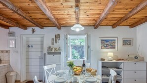 Un coin repas avec une table ronde dressée pour quatre personnes, des chaises blanches, un plafond en bois, une fenêtre avec vue, une radio et une bibliothèque.