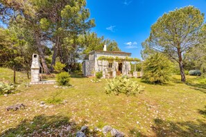 Ein Steinhaus mit Steinkamin, umgeben von Bäumen und einer Rasenfläche mit Steinen.