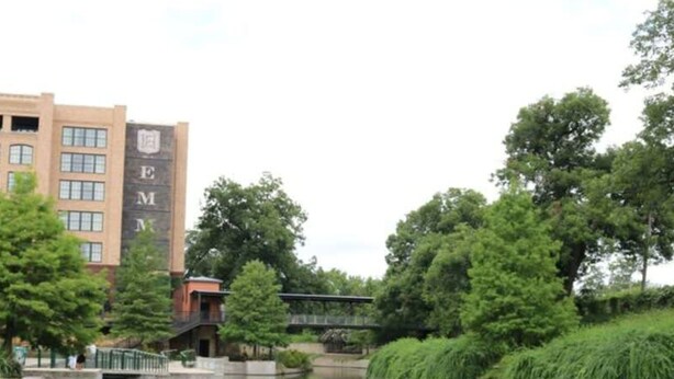 A building with a large 'EM' logo, surrounded by greenery and a calm water body. - Amazing Fully Fenced Home Only 1 7 mi to Downtown (San Antonio)