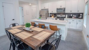 A modern kitchen with white cabinets, a central island, and a dining area with a wooden table and chairs. - Gorgeous 3 BR 2 BA Near Amazing Downtown (San Antonio)