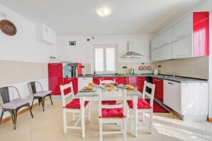 Una cocina moderna con armarios blancos, una encimera roja y un comedor con sillas blancas y cojines rojos.