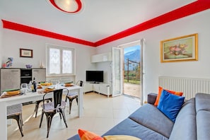 Una sala de estar moderna con un sofá gris, una mesa de comedor con sillas, un televisor y una zona de cocina.