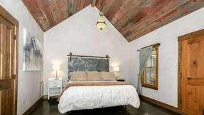 Une chambre avec un grand lit, des poutres apparentes en bois au plafond et une table de chevet avec une lampe.
