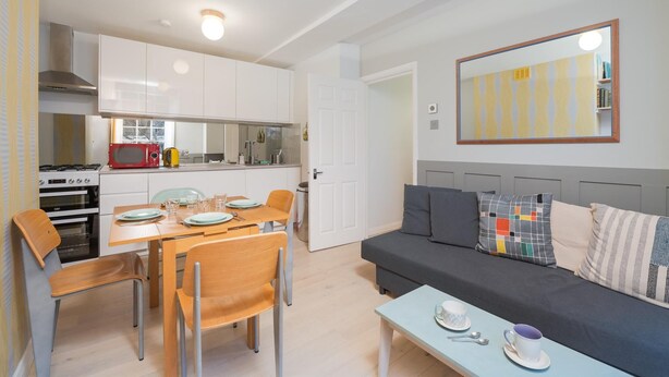 Ett kompakt bostadsutrymme med ett litet kök, en matplats och en soffa med kuddar.