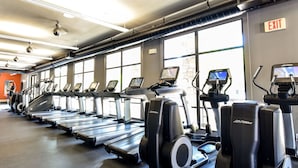 Une salle de sport équipée de tapis de course et d’appareils elliptiques, dotée de grandes fenêtres et d’un panneau indiquant la sortie.