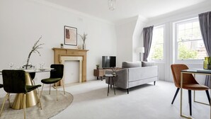 Een moderne woonkamer met een open haard, een bank, een televisie en een eethoek met stoelen en een tafel.