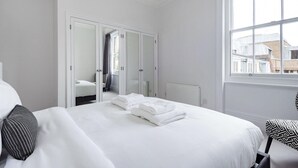 Een hotelkamer met een groot bed, een kledingkast en een raam met uitzicht op gebouwen.