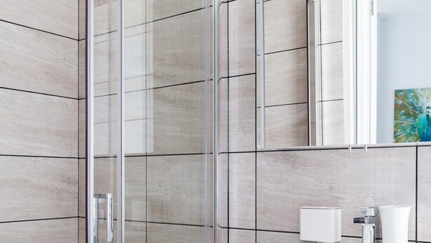 A modern bathroom with a glass shower enclosure, a white sink, and a mirror above it. - Luxury 1-bedroom Suite Next to Oxford Street (London)
