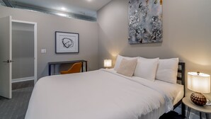 A hotel room with a large bed, a desk, a chair, a painting, and a lamp. - Des Moines Beautiful 2BD 2BA Downtown Apartment (Des Moines)