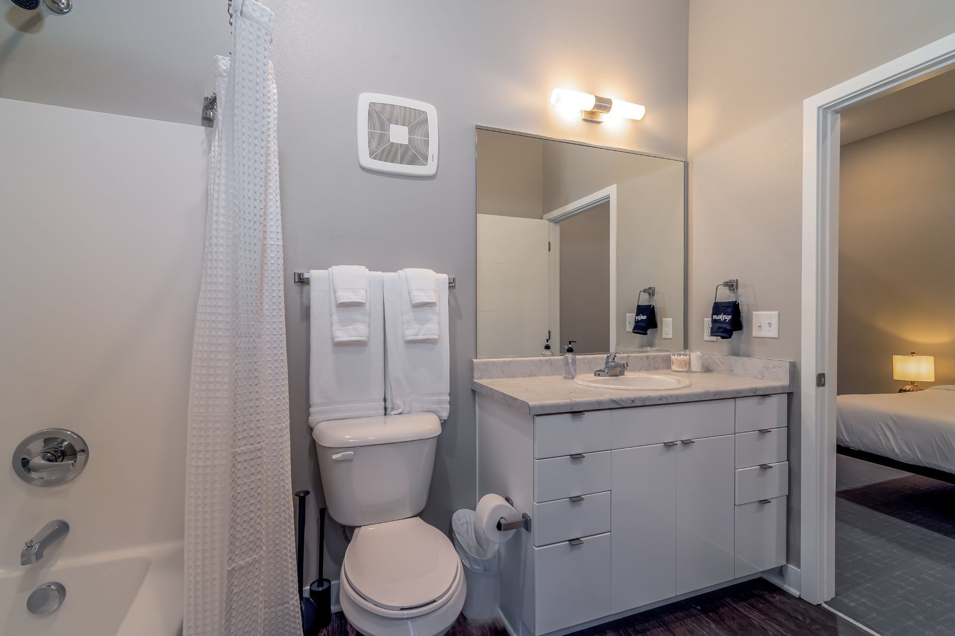 A modern bathroom with a toilet, sink, and mirror. There are towels hanging on the wall and a shower curtain.