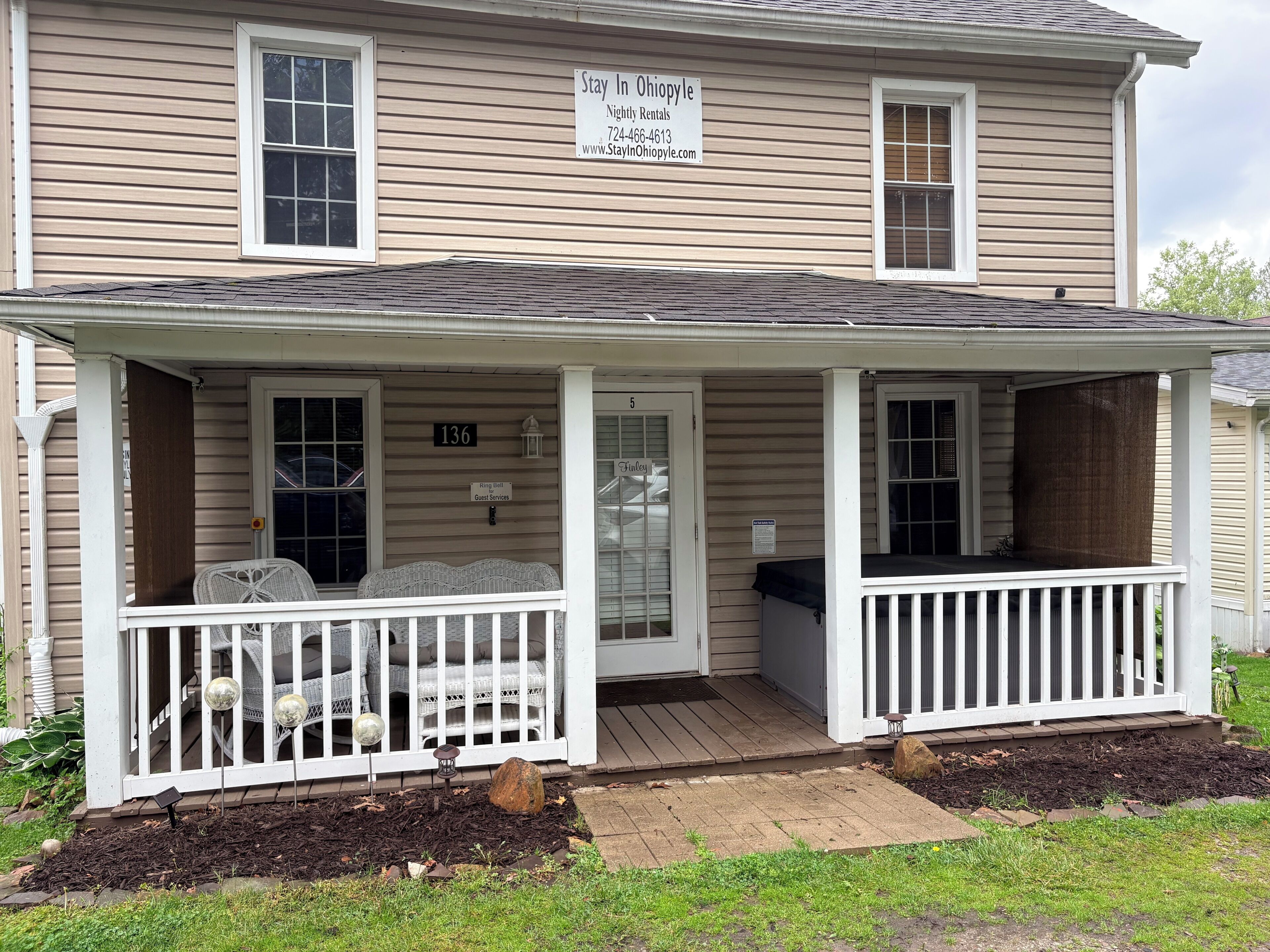A two-story house with a covered porch, a sign for nightly rentals, and a guest services sign.