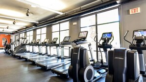 Kuntosali, jossa on useita juoksumattoja ja crosstrainer-laitteita, suuret ikkunat ja uloskäynnin opastekyltti.
