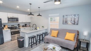 A modern kitchen with a central island, bar stools, and a grey sofa with yellow cushions. - Cozy and Lovely 2BR 1BA Apt B Near Lively Downtown (San Antonio)
