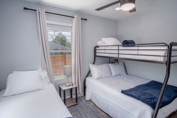 Una habitación individual con una cama nido, una mesita de noche pequeña, una ventana con cortinas y un ventilador de techo.