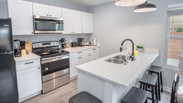 A modern kitchen with white cabinetry, stainless steel appliances, and a central island with bar stools. - Cozy and Lovely 2BR 1BA Apt B Near Lively Downtown (San Antonio)
