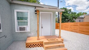 A small building with a white door, a window with a screen, and a wooden deck leading to the door. - Cozy and Lovely 2BR 1BA Apt B Near Lively Downtown (San Antonio)