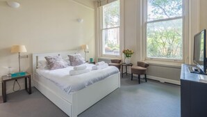 Een hotelkamer met een groot bed, twee nachtkastjes, een stoel, een tafeltje met een bloemenvaas en een televisie.