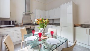 Een moderne keuken met witte kastjes, een magnetron, kookplaat en een eethoek met een glazen tafel gedekt voor twee personen.
