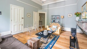 Een woonkamer met een bank, stoelen, een bijzettafeltje en een boekenkast.