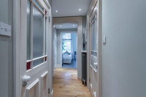 Ein schmaler Flur mit Holzboden, der in ein Schlafzimmer mit Bett und Heizkörper führt.