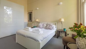 Een keurig opgemaakt slaapkamer met een bed, nachtkastjes, lampen en een vaas met bloemen.