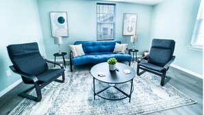 A modern living room with a blue sofa, two black chairs, a coffee table, and a ceiling fan. - Fascinating 1BR 1 BA Near Festive DT and Riverwalk (San Antonio)