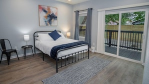 A bedroom with a bed, a chair, a small table, a ceiling fan, a window with curtains, and a view of the outdoors. - Your Dream Stay 4BR 2BA Near Downtown Riverwalk (San Antonio)