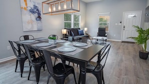 A dining area with a rectangular table set for six, surrounded by black chairs. There is a ceiling fan above and a modern light fixture hanging from the ceiling. - Your Dream Stay 4BR 2BA Near Downtown Riverwalk (San Antonio)