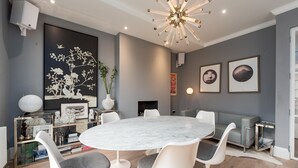 A modern dining area with a marble table, white chairs, and a unique ceiling light fixture. - Maida Vale Elegance (London)