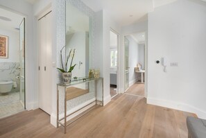 A modern bathroom with a glass shower enclosure, a marble-tiled sink, and a decorative vase with orchids. - Maida Vale Elegance (London)