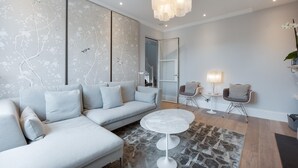 A modern living room with a grey sectional sofa, a round white table, and a patterned rug. - Maida Vale Elegance (London)