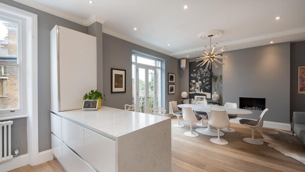 A modern kitchen with a large island, white cabinetry, and a dining area with a round table and white chairs. - Maida Vale Elegance (London)