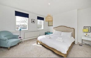 Classic bedroom with a large bed, two windows, and a comfortable armchair.