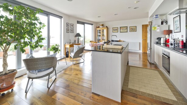 A modern kitchen with a central island, wooden flooring, and a dining area with wicker furniture.
