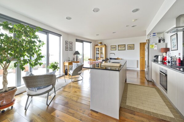 A modern kitchen with a central island, wooden flooring, and a dining area with wicker furniture.