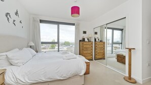 A bedroom with a large bed, wooden dresser, and a sliding glass door leading to another room. - Putney Rooftops (London)