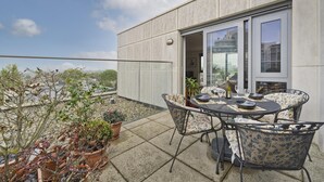 A terrace with a table and chairs, potted plants, and a view of the city.