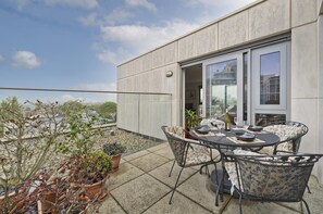A terrace with a table and chairs, potted plants, and a view of the city.