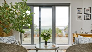 A modern living room with a glass door leading to a balcony, wicker furniture, and a view of the cityscape.