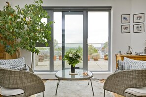A modern living room with a glass door leading to a balcony, wicker furniture, and a view of the cityscape.