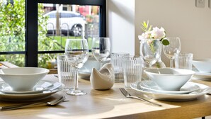 A dining table set with white plates, bowls, and glasses, with a vase of flowers on the right. - Greenwich Perfection (London)