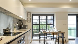A modern kitchen with a large window, a dining area with chairs, and a view of the outside. - Greenwich Perfection (London)