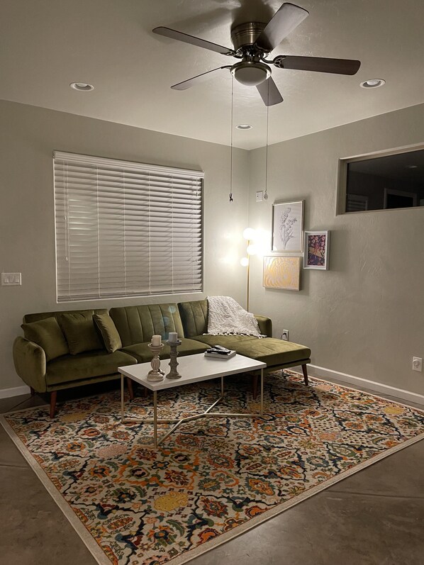A living room with a green sofa, a white coffee table, a patterned rug, and a ceiling fan. - Immaculate guesthouse in the NW Tucson desert...yet close to everything! (Tucson)