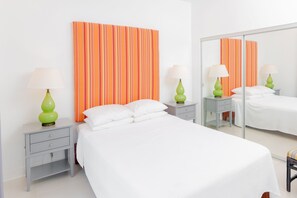 A hotel room with a large bed, two nightstands with lamps, a mirror, and a striped curtain. - Colibri Court (Jolly Harbour)