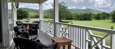 A covered outdoor seating area with wicker furniture and a view of a green landscape.