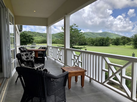 A covered outdoor seating area with wicker furniture and a view of a green landscape.