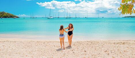 A beach with a clear sky and calm sea, featuring two people standing on the sand.