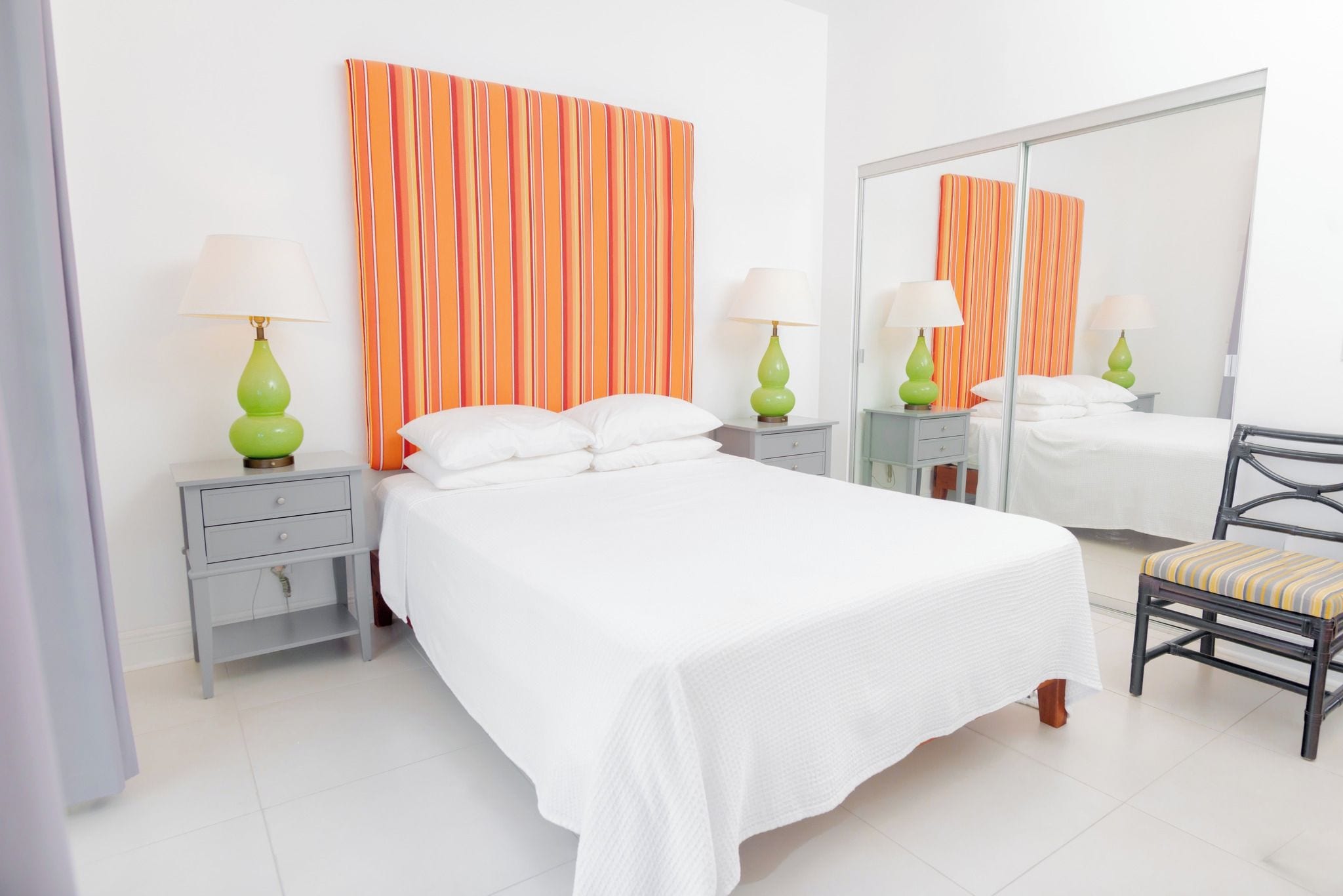 Una camera d'albergo ordinata con un letto grande, due comodini con lampade, una sedia e uno specchio.