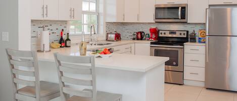 A modern kitchen with white cabinetry, stainless steel appliances, and a central island with seating.